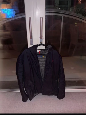 Mörkblå packbar dunjacka Polo Ralph Lauren - Snygg mörkblå dunjacka från Polo Ralph Lauren med röd logga på bröstet och diskret 'PACKABLE'-text. Jackan är lätt, quiltad och har en grå insida. Perfekt för kalla vinterdagar och enkel att packa ner i väskan.