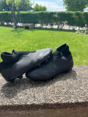 Svarta Adidas fotbollsskor utan snörning - Säljer ett par helsvarta Adidas fotbollsskor med ny pris på 3000kr elite, skorna har strumpliknande skaft och utan snörning. Skorna har en modern, slimmad design och mönstrad ovansida i syntetmaterial för bra bollkontroll. Dobbarna är anpassade för spel på gräsplan och konstgräs(hybrid)