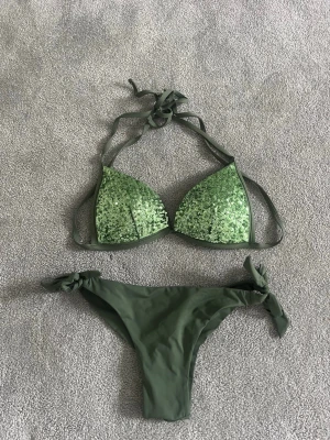 Grön bikini med paljetter och knyt - Bikini köpt i spanien i vintras, endast använd 1 gång🥰 Både överdel och underdel storlek S! Super snygg och skön! Säljer då den tyvärr är för liten…