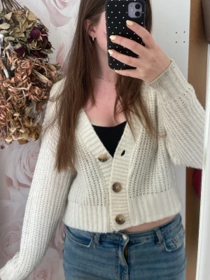 Vit stickad kofta från Boohoo - Supermysig vit stickad kofta från Boohoo med stora bruna knappar och djup v-ringning. Koftan är croppad och har långa ärmar samt bred ribbad kant nedtill och vid ärmsluten. Perfekt att slänga över ett linne eller t-shirt❣️