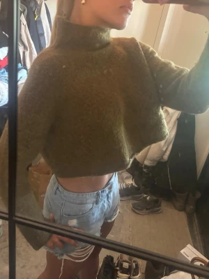 Olivgrön croppad stickad polotröja - Säljer en olivgrön croppad stickad tröja med polokrage och långa ärmar. Tröjan har en mysig och fluffig känsla, perfekt för lager-på-lager och trendiga outfits. Passar dig som gillar en avslappnad men stilren look.