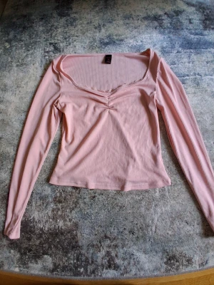 Rosa ribbad långärmad topp Bik Bok - Söt ljusrosa ribbad topp från Bik Bok med lång ärm och v-ringning. Toppen har en liten rynkdetalj framtill och spetskant vid halsen. Perfekt att styla med jeans eller kjol för en trendig look.
