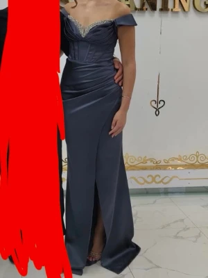 Mörkblå axelbandslös balklänning - Elegant mörkblå långklänning med offshoulder-design och glittrig detalj vid bysten. Klänningen har en slits framtill och figurnära passform, perfekt för bal eller fest. Tillverkad i ett glansigt material som ger en lyxig känsla. Den är sydd om så den är tightare. Den är strl 40 men sydd om till 36. Endast använd i ett par timmar.