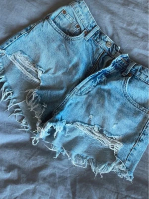 Jeansshorts Zara - Säljer ett par ljusblåa jeansshorts. Shortsen har slitna detaljer framtill och klassiska fickor både fram och bak.