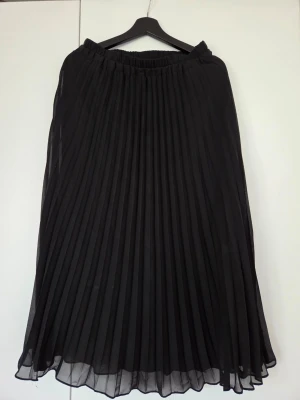 Svart plisserad långkjol från Monki - Säljer en svart långkjol från Monki med snygg plisserad design och elastisk midja. Kjolen har ett luftigt och flowy tyg som ger en stilren look. Perfekt att matcha med en crop top eller stickad tröja.