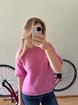 Rosa stickad t-shirt från Dobber - Säljer en söt rosa stickad t-shirt med korta ärmar och rund hals. Tröjan har en mjuk och fluffig känsla. Perfekt för lager-på-lager och ger en trendig look till jeans eller kjol.
