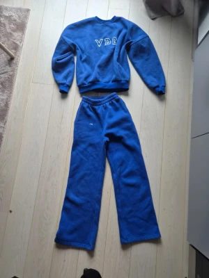 Blått loungewear-set från Enderby's - Mysigt blått loungewear-set från Enderby's med sweatshirt och matchande byxor. Tröjan har trycket 'VDE' framtill och byxorna har resår i midjan. Det är storlek xs i bycorna och xs/s i tröjan 