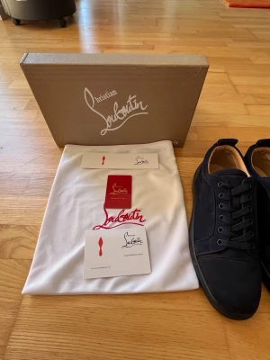 Svarta sneakers från Christian Louboutin - Snygga svarta sneakers från Christian Louboutin med klassisk låg siluett. Skorna har ovandel i mocka och detaljer i svart läder. Kommer med originalkartong, dustbag och äkthetskort. Perfekta för dig som gillar exklusiva och stilrena sneakers.