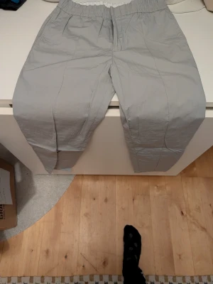 Grå kostymbyxor från Tiger of Sweden - Snygga grå kostymbyxor från Tiger of Sweden med elastisk midja och klassisk passform. Byxorna har diskreta pressveck och dragkedja fram. Perfekta för en stilren look.