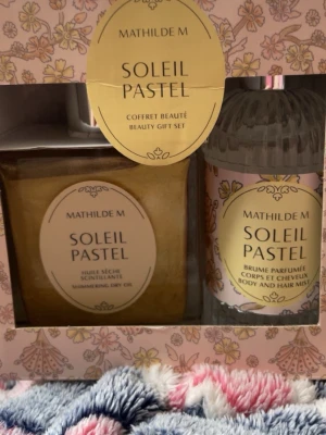 Mathilde M Soleil Pastel Beauty Set - Mathilde M Soleil Pastel coffret beauté innehåller en skimrande kroppsolja och en parfymmist för kropp och hår. Setet kommer i en dekorativ förpackning med blommigt mönster i pastellfärger. Perfekt för dig som vill ha en lyxig och fräsch känsla.