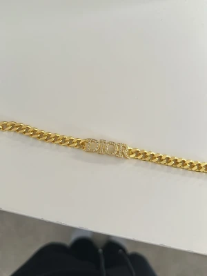 Guldarmband från Dior med pärlor - Snyggt guldarmband från Dior med kedjelänk och Dior-logga i mitten dekorerad med små glittrande pärlor. Armbandet har även en liten rund bricka med Dior ingraverat vid låset. Perfekt accessoar för att lyfta din stil.