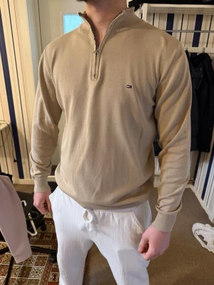 Beige halvzip-tröja Tommy Hilfiger - Snygg beige långärmad halvzip-tröja från Tommy Hilfiger med liten logga på bröstet. Tröjan har ribbade muddar och krage med dragkedja. Perfekt för en clean och stilren look. Materialet känns mjukt och bekvämt. Nypris: 1200