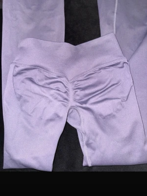 dfyne impact flare pants - Säljer ett par lila leggings med scrunch-detalj bak och bred, ribbad midja. De är sömlösa och har en tight passform som framhäver formerna. Perfekta för gymmet eller chill hemma. Materialet känns stretchigt och mjukt mot huden.