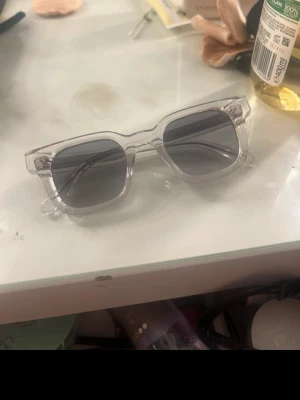 Solglasögon från Chimi - Säljer ett par stilrena solglasögon från Chimi med transparent båge och mörkgrå, fyrkantiga linser. Snygg och modern design som passar till alla outfits. Kommer med originalförpackning.