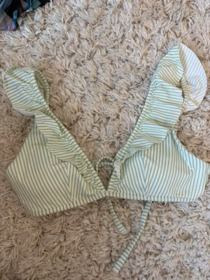 Randig bikiniöverdel med volang - Söt bikiniöverdel med ljusgröna och vita ränder, volangdetaljer längs axelbanden och knyt i ryggen. Perfekt för sommaren och strandhäng. Bekväm passform och trendig look. Aldrig använda!!
