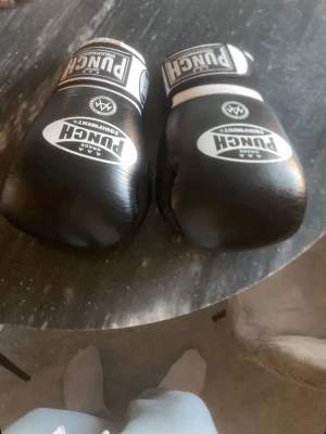 Boxningshandskar Punch - Säljer ett par svarta boxningshandskar från Punch Equipment med vita detaljer och tydlig logga. Handskarna har kardborreband vid handleden för enkel justering och sitter skönt på handen. Perfekta för träning eller sparring.