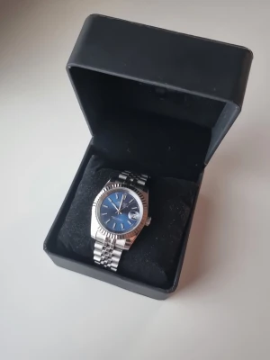 Seiko - Säljer nu en riktigt häftigt Seiko mod klocka i datejust stil. 39-42mm. Den har en marinblå sunburst urtavla och ett jubilee armband. Dessutom har den en open case back design allstå kan man se urverket från baksidan. Klockan har en automatisk NH35A seiko urverk. Medföljer extra länkar och box (i bild 1). Dock har den lite repor då den vart använd ( svårt att få med på bild), dock syns det i princip bara på spännet. Inget som märks såvida man inte kolar nära. Därav priset.
