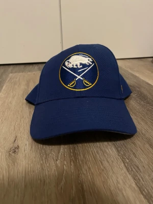 Blå Buffalo Sabres keps från '47 - Snygg blå keps med Buffalo Sabres-logga broderad framtill och gul '47-detalj på sidan. Klassisk böjd skärm och justerbar passform. Perfekt för hockeyfans som vill visa sitt lagstöd. Tillverkad i slitstark bomull. Pris kan absolut diskuteras.   
