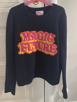 Mörkblå stickad tröja From Future XS - Cool svart stickad tröja från From Future med färgglad text 'MAGIC FUTURE' i rosa och gul på bröstet. Tröjan har rund halsringning och långa ärmar. Perfekt för dig som gillar statement-plagg och vill sticka ut. Den har ett pyttelitet hål vid halsen men man ser det inte alls när man har på sig den!