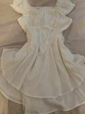 Vit kortklänning med volangärmar - Supersöt vit kortklänning med volangärmar och offshoulder-design. Klänningen har en luftig kjol och markerad midja som ger en feminin siluett. Perfekt för varma dagar och somriga tillfällen. Tillverkad i ett lätt och mjukt tyg som känns skönt mot huden. Även perfekt som basplag till halloween utstyrsel.