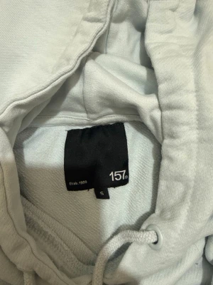 Ljusblå hoodie från 157 - Ljusblå hoodie från 157 med klassisk huva och dragsko. Tillverkad i mjukt bomullsmaterial som känns skönt mot huden. Hoodien har en enkel och stilren design utan tryck eller mönster, perfekt för en avslappnad look.