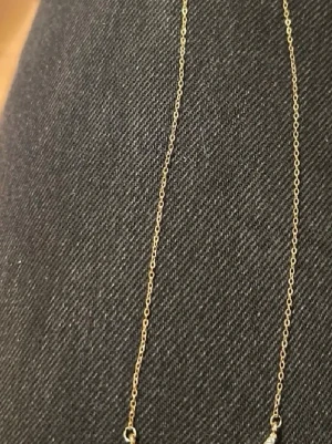 Halsband liknar Zadig  - Snyggt halsband i guldton med ett hänge format som två vingar täckta av små glittrande stenar. Kedjan är tunn och elegant, perfekt för att ge din outfit lite extra bling. Inget synligt märke på halsbandet. Materialet ser ut att vara metall med stenar.