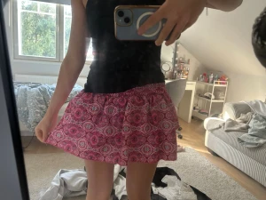 Rosa mönstrad kortkjol - Säljer en rosa kortkjol med vitt och svart mönster. Kjolen har en luftig passform och resår i midjan, vilket gör den bekväm och enkel att bära. Perfekt för varma dagar och ger en färgglad touch till din outfit.