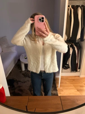 Vit  kofta - Mysig vit kofta med fluffig textur och rak passform. Koftan har långa ärmar och är öppen framtill med en knapp där uppe. 