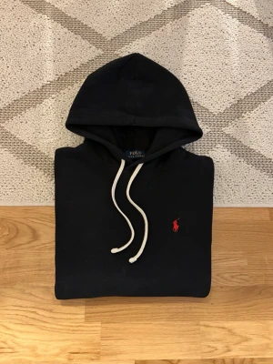 Svart Polo Ralph Lauren Fleece Hoodie - Hej! 👋 Säljer en riktigt fräsch Polo Ralph Lauren hoodie i storlek S (herrstorlek 170/92A). 💎 Svart färg som funkar till allt ✨ Nyskick och ser knappt använd ut, se bilderna för detaljer 🎉 Sitter riktigt bra och har en skön passform 👕 Klassisk röd broderad pony-logga på bröstet 🐎 QR-kod för äkthetsverifiering och alla tvättlappar sitter kvar ✅ Fraktar snabbt! 🚚📦 Hör av er vid frågor! 💬💯