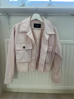 Ljusrosa jeansjacka från Bik Bok - Ljusrosa jeansjacka från Bik Bok i storlek XS. Jackan har klassisk krage, stora bröstfickor med knapp och raka ärmar. Perfekt för dig som vill ha en cool och trendig look med en touch av pastell. Materialet är jeans och jackan har en boxy fit.