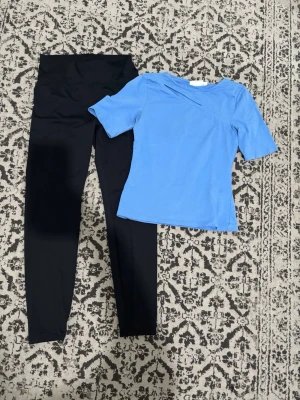 Svart och blått  - Snyggt set med svarta höga leggings och en blå topp med kort ärm och asymmetrisk halsringning. Perfekt för dig som gillar enkel men trendig stil. Materialet ser ut att vara mjukt och stretchigt för skön passform.