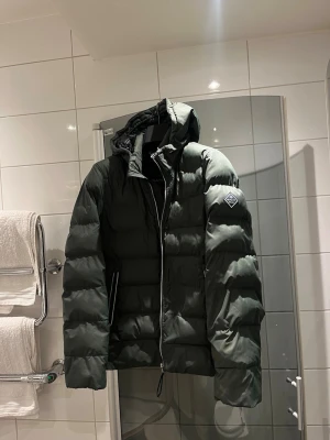 Mörkgrön dunjacka från Gant  - Snygg mörkgrön lättvikts dunjacka från GANT med huva och dragkedja framtill. Jackan har två sidofickor med dragkedja och en patch med logga på ärmen. Perfekt vårjacka och ger en riktigt modern look. Storlek small. Jättebra skick. Jag är 177 cm lång och väger 82 och den sitter bra på mig. Nypris 3600 kr 