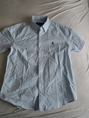 LINEN SHORT SLEEVE SPORT - Skjorta - office blue - Klassisk ljusblå skjorta från Polo Ralph Lauren med korta ärmar och button-down krage. Skjortan har knappar framtill och den ikoniska logotypen broderad på bröstet. Perfekt till jeans eller chinos för en clean look.