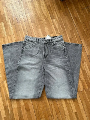 Gråa wide leg jeans med tvättad look - Säljer ett par gråa jeans med extremt wide leg och cool tvättad finish. Jeansen har klassisk femficksdesign, bälteshällor och knappgylf. Perfekta för dig som gillar statement-plagg och oversized stil. Helt nya