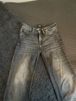 Grå high waist jeans från ONLY - Säljer ett par grå jeans från ONLY. Jeansen har utsvängda ben med slitsar vid bensluten och klassisk femficksmodell. Perfekta för en avslappnad och trendig look. Insydda mellan benen. 