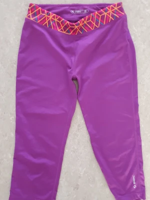 Träningstights - Snygga lila träningstights från SOC med färgglad midjeresår i mönster av rosa, gult och blått. Tightsen är i stretchigt material och är perfekt för gym eller löpning.