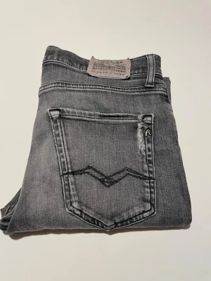  Replay - Snygga grå jeans från Replay med klassisk femficksdesign och coola detaljer på bakfickan. Jeansen har en tvättad look och är tillverkade i mjukt denimtyg med stretch för extra komfort. Perfekta för en avslappnad och trendig stil.