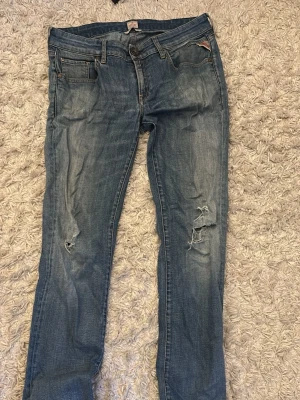 Blå slitna jeans med hål - Säljer ett par blå replay jeansmed slitningar och hål på knäna. Jeansen har klassisk femficksmodell, normal midja, bara atta skriva om funderingar framkommer! Obs hål i skrevet men enkelt att fixa. Storleken står på men är 31/32