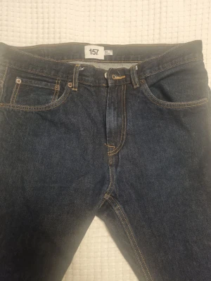 Mörkblå jeans från 157, rak modell - Klassiska mörkblå jeans från 157 med raka ben och femficksmodell. Jeansen har kontrastsömmar i gult och är tillverkade i slitstarkt denimtyg. Perfekta för en avslappnad och stilren look.