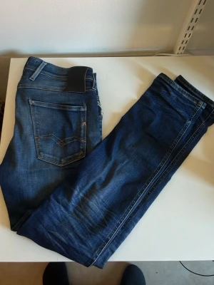 Mörkblå jeans från Replay - Snygga mörkblå jeans från Replay med klassisk femficksmodell och diskreta slitningar framtill. Jeansen har raka ben och detaljerade sömmar på bakfickorna. Tillverkade i ett mjukt denimtyg som sitter skönt hela dagen, priset kan diskuteras.