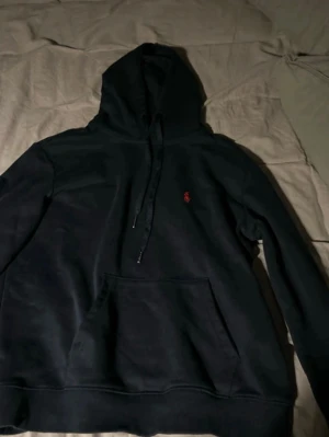 Mörkblå hoodie från Polo Ralph Lauren - Säljer en mörkblå hoodie från Polo Ralph Lauren med klassisk röd logga broderad på bröstet. Hoodien har huva och en stor magficka framtill. Perfekt för dig som gillar stilrena och tidlösa plagg. Är i medium (M) i barn storlek passar ungefär till barn som 158-162