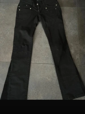Svarta bootcut jeans  - Snygga svarta jeans från Link med raka ben och klassisk femficksdesign. Jeansen har silverfärgade nitar och detaljerade sömmar på bakfickorna. 