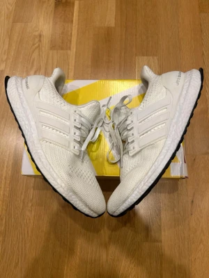 Vita Adidas Ultra Boost sneakers - Säljer ett par vita Adidas Ultra Boost sneakers med stickad ovandel i mesh för grym komfort och andningsförmåga. Klassiska tre ränder på sidan, vit sula med Boost-dämpning och svart yttersula. Perfekta för dig som gillar stilrena och sportiga skor.  Väldigt bra skick (kolla bilder). Passar storlek 43,5 PRISET KAN DISKUTERAS
