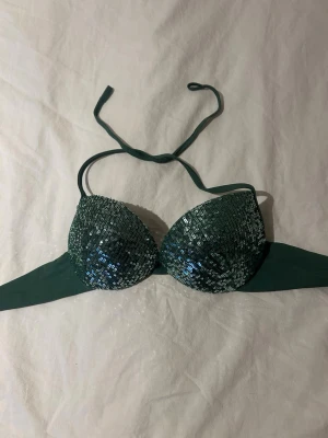 Grön bikiniöverdel med paljetter Calzedonia - Supersnygg grön bikiniöverdel från Calzedonia med glittriga paljetter på kuporna. Bikinin har halterneck knyt och vadderade kupor för extra stöd. Perfekt för dig som vill sticka ut på stranden!