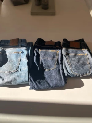 Tre par jeans från Nudie Jeans Co - Säljer tre par jeans från Nudie Jeans Co i olika blå tvättar. Alla har klassisk femficksdesign, kontrastsömmar och läderpatch bak i midjan. Perfekta för dig som gillar stilrena och tidlösa jeans i denim.