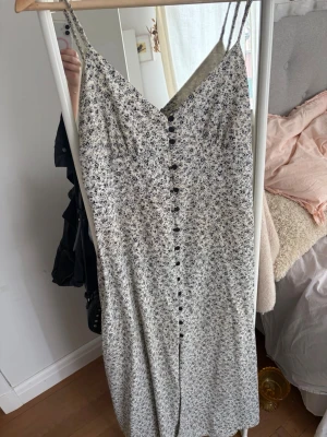 Långklänning  - En vit långklänning med svarta blommor på, strl L men sitter som en M!