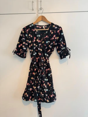 Blommig omlottklänning - Väldigt fin blommig omlottklänning som knyts i midjan. Inga tecken på användning! Något glansigt material/satinaktigt.
