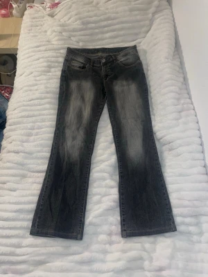 Bootcut svarta jeans med slitningar - Snygga svarta bootcut jeans med slitna detaljer framtill och baktill. Klassisk femficksmodell med låg midja och lätt utsvängda ben. Jeansen har en tvättad look som ger en cool och avslappnad vibe. Perfekta till sneakers eller boots.