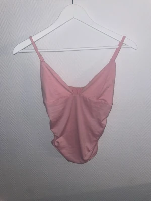 Rosa linnetopp med smala axelband - Söt rosa linnetopp med smala justerbara axelband och lätt rynkad effekt framtill. Toppen har en v-ringad skärning och är tillverkad i ett mjukt, stretchigt material som känns bekvämt mot huden. Perfekt för varma dagar eller att styla lager på lager.