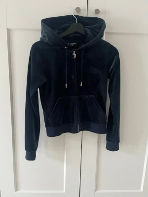 Mörkblå zip,  Juicy Couture - Mjuk och lyxig mörkblå hoodie från Juicy Couture i velourmaterial. Dragkedja framtill, två fickor och justerbar huva med snören. Klassisk passform och ribbade muddar vid ärmslut och nederkant. Perfekt för en chill och trendig look. Fråga vid fundering, öppen får prisförslag
